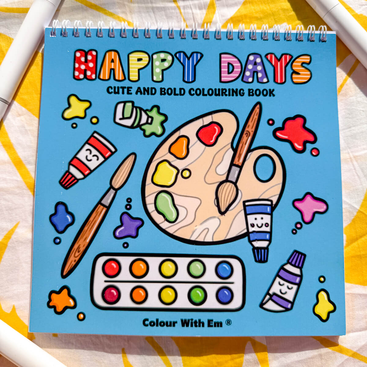 "Happy Days" Cute and Bold Colouring Book by Colour With Em, featuring a vibrant cover with an artist's palette, paintbrushes, and colourful paint splashes, designed for creative fun.